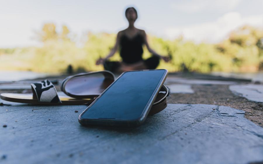blurred woman in background meditating, cell phone in the foreground