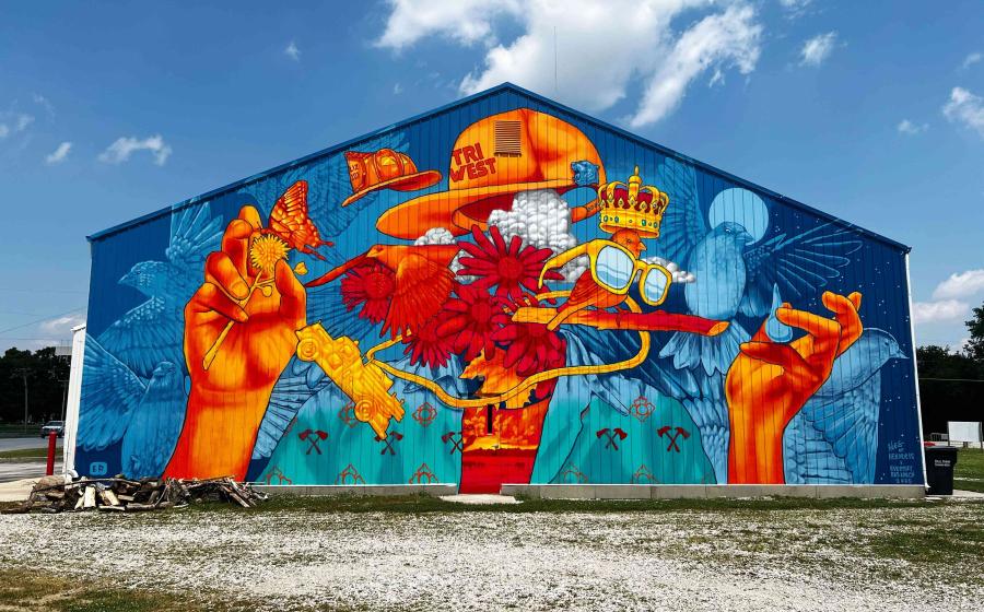 Colorful blue barn with an enormous mural of art on the face of it.