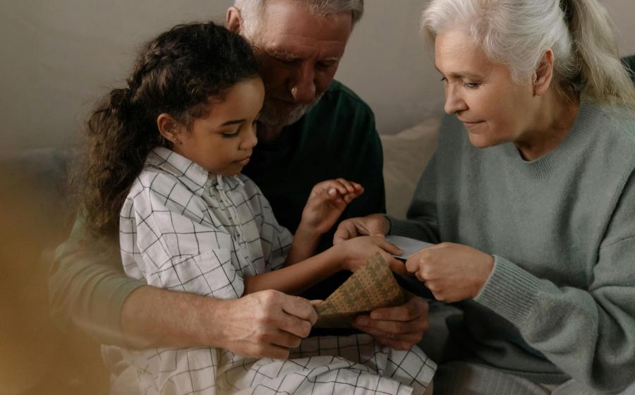Two grandparents helping a granddaughter with folding paper