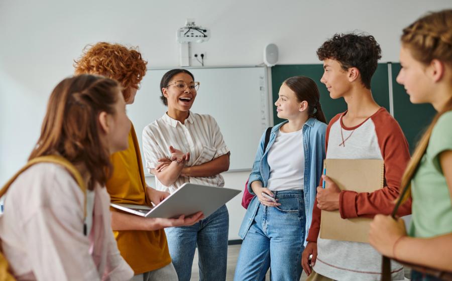 Happy african american teacher talking to teenage students in classroom, back to school concept