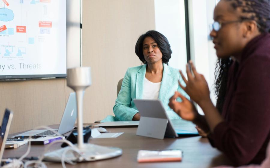 Two women in a business meeting; the closer one is out of focus and the far one is intently listening to her