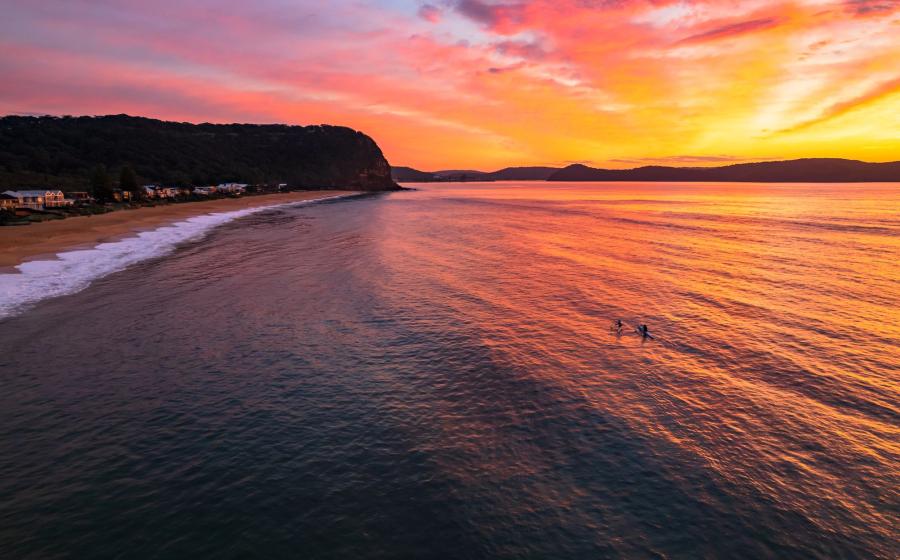 Sunrise at the seaside with cloud filled sky and two people in surf ski kayaks from Pearl Beach on the Central Coast, NSW, Australia.