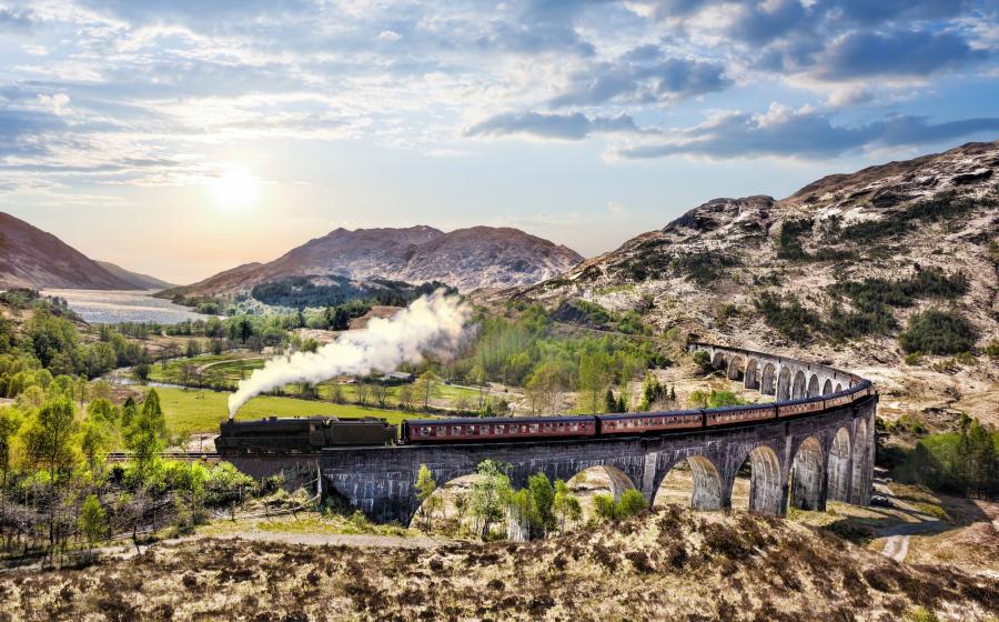 Glenfinnan Railway Viaduct in Scotland with the Jacobite steam train against sunset over lake