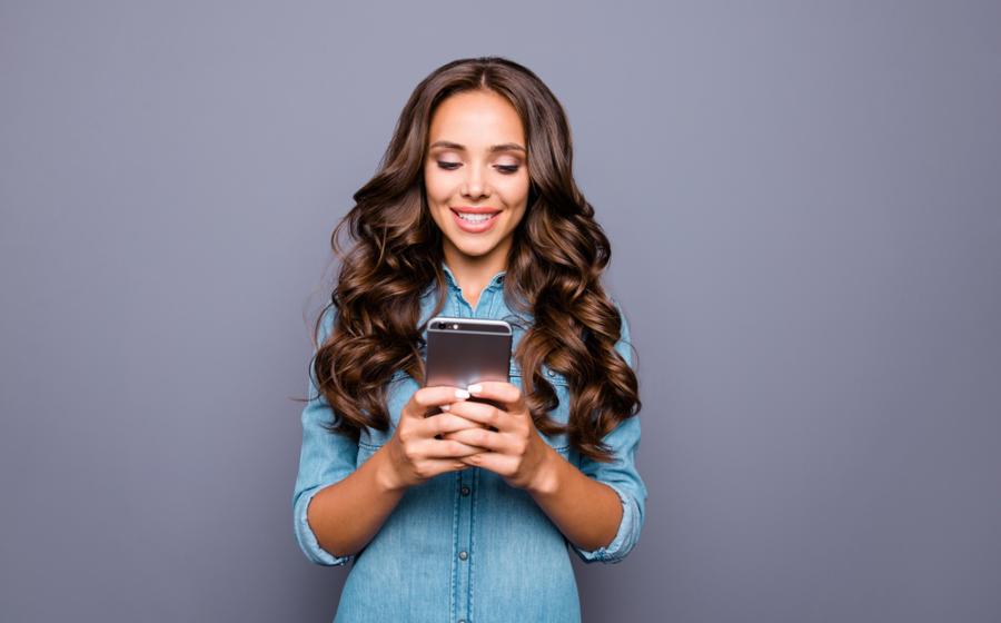 Cropped image of a smiling woman using mobile phone while drinking take away coffee outdoors