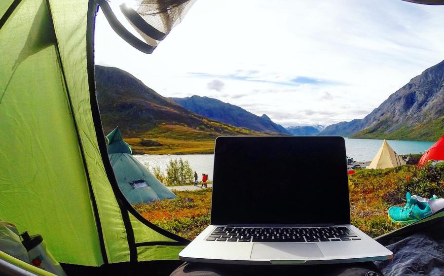 Working on a laptop while in a tent looking at mountains and a lake