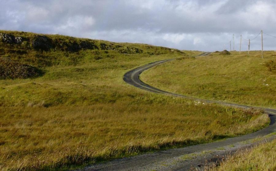 Curvy road in Ireland winding through green hills, with a cloudy grey sky