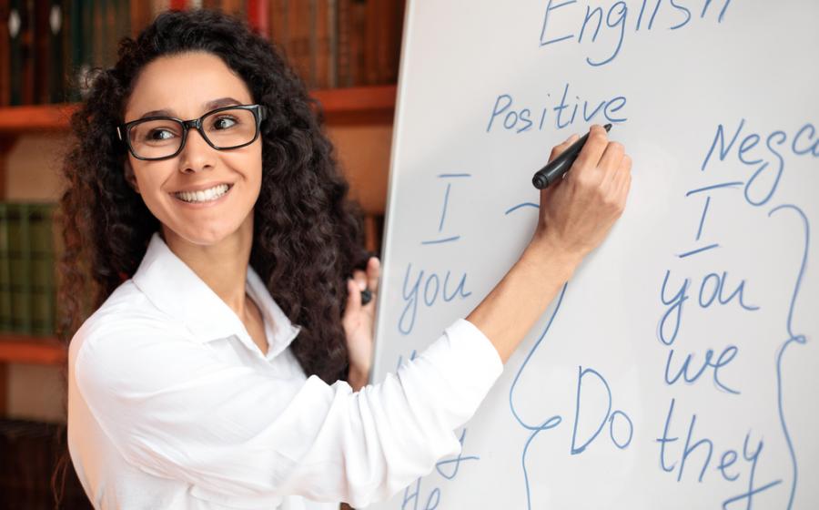 Smiling female teacher writing at whiteboard, explaining rules