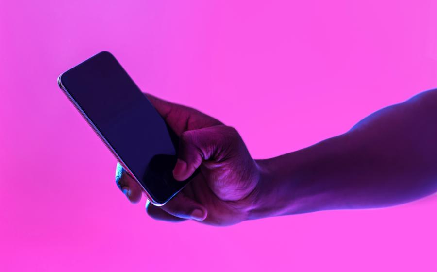 Unrecognizable black guy using cellphone with blank screen in neon light, free space