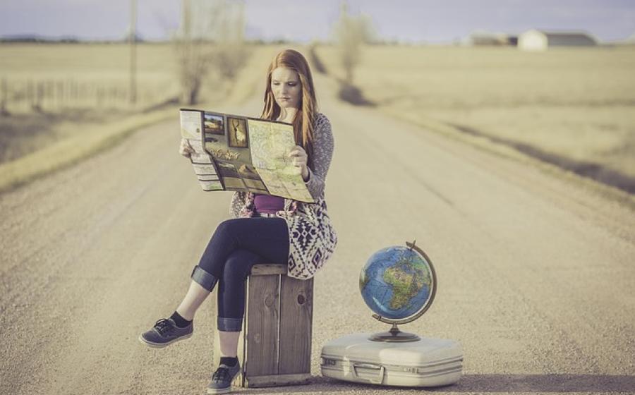Woman sitting on a suitcase reading a map in the middle of an empty road