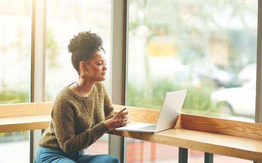 Woman on her laptop at a cafe, sunshine coming in through the large glass windows