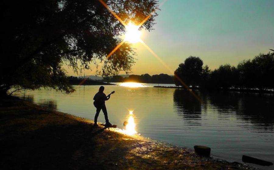 sunset on a river, guitar player standing on river bank