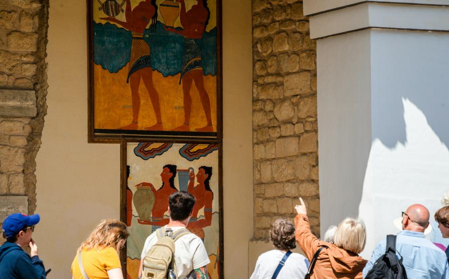 People observe ancient minoan frescoes on a wall