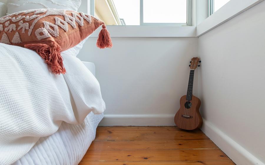 ukelele on the floor next to a bed and windows