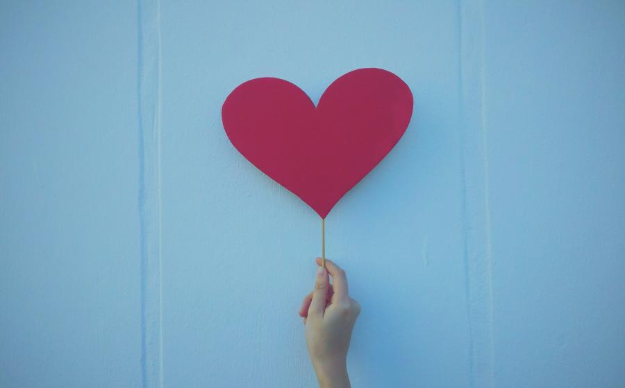 hand holding a red heart against a blue wall