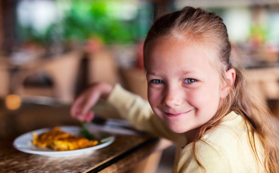 Casual portrait of adorable little girl enjoying meal at restaurant