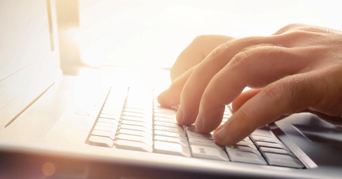 hands typing on a laptop, sunshine in the back
