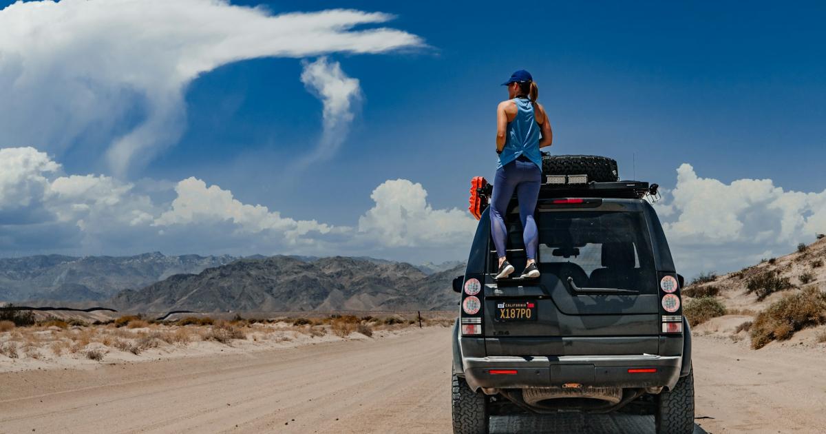 woman standing on her vehicle in the desert and mountains