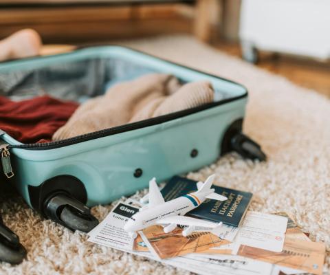 Green suitcase open on a carpet. It is filled with clothes and there are papers and passport next to it