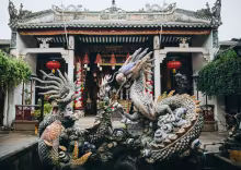 A vibrant dragon sculpture is set in a traditional courtyard in Vietnam. Lush greenery frames the intricate details of the artwork, featuring earthy tones and vivid colors.